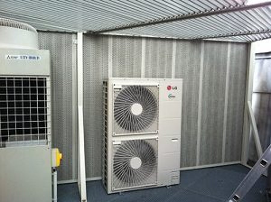 Une unité extérieure de climatisation LG à deux ventilateurs est installée dans un local technique grillagé, à côté d'un autre équipement.