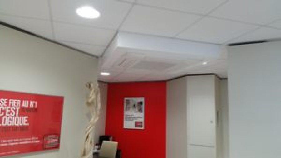 Intérieur d'un bureau avec un faux plafond abritant une unité de climatisation, des murs rouges et blancs et une affiche rouge à gauche.